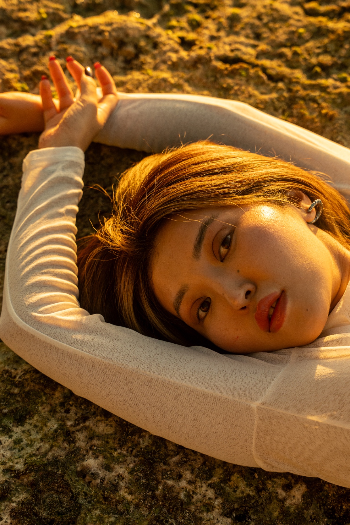 Close beauty crop on warm volcanic rock, red lacquered nails catching last light