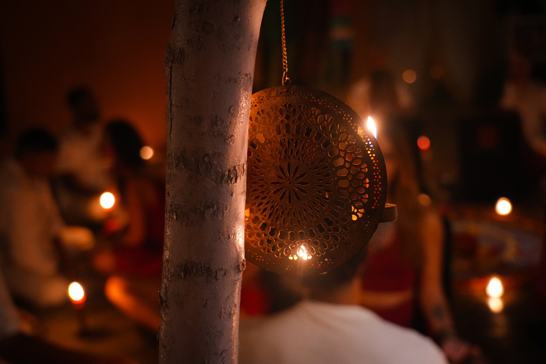 Pierced brass lantern glowing on a tree trunk above the ceremony