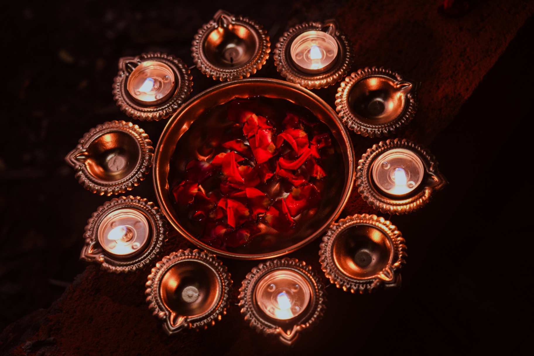 Copper bowl with rose petals encircled by glowing diyas