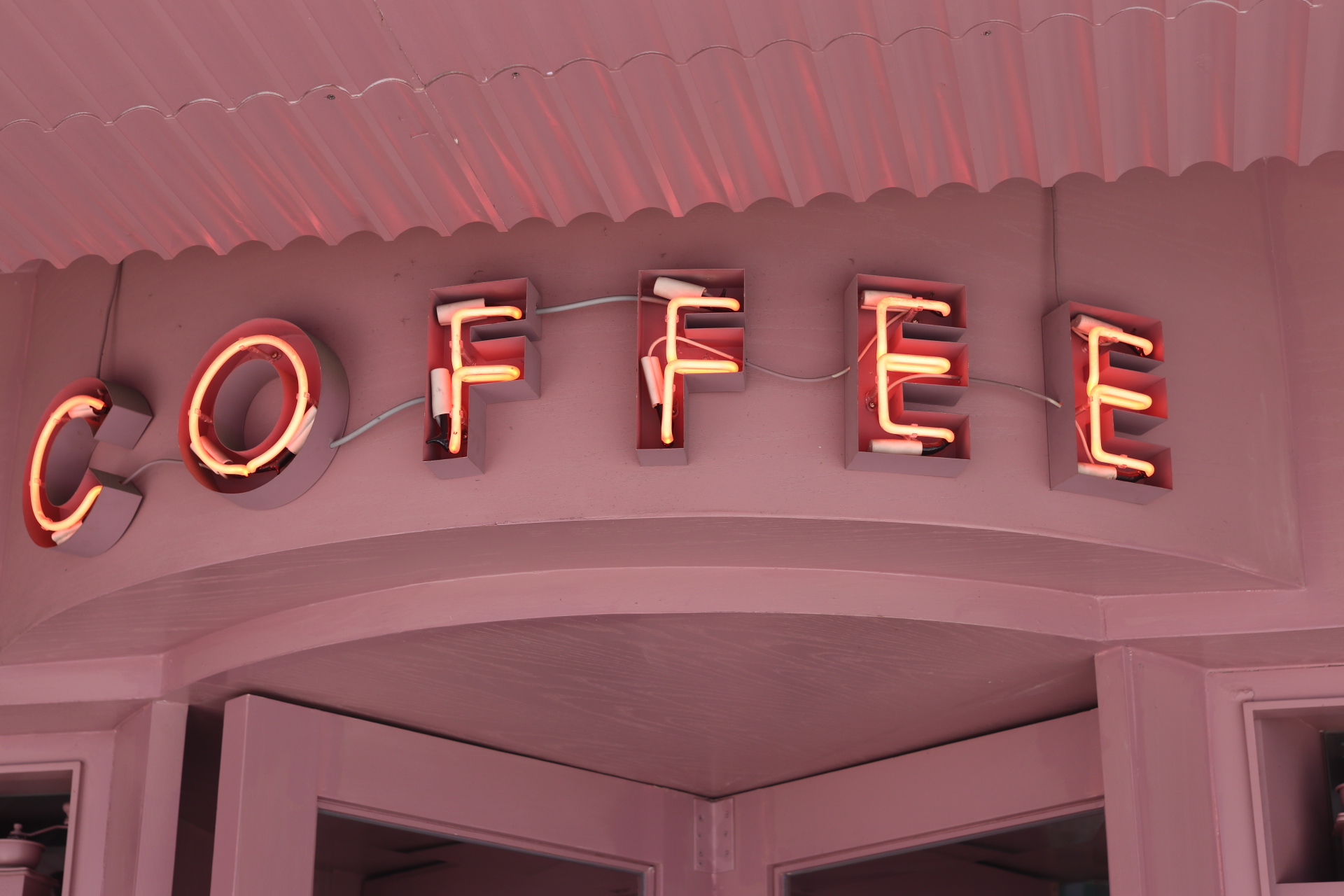 Neon COFFEE sign glowing above a pink scalloped awning