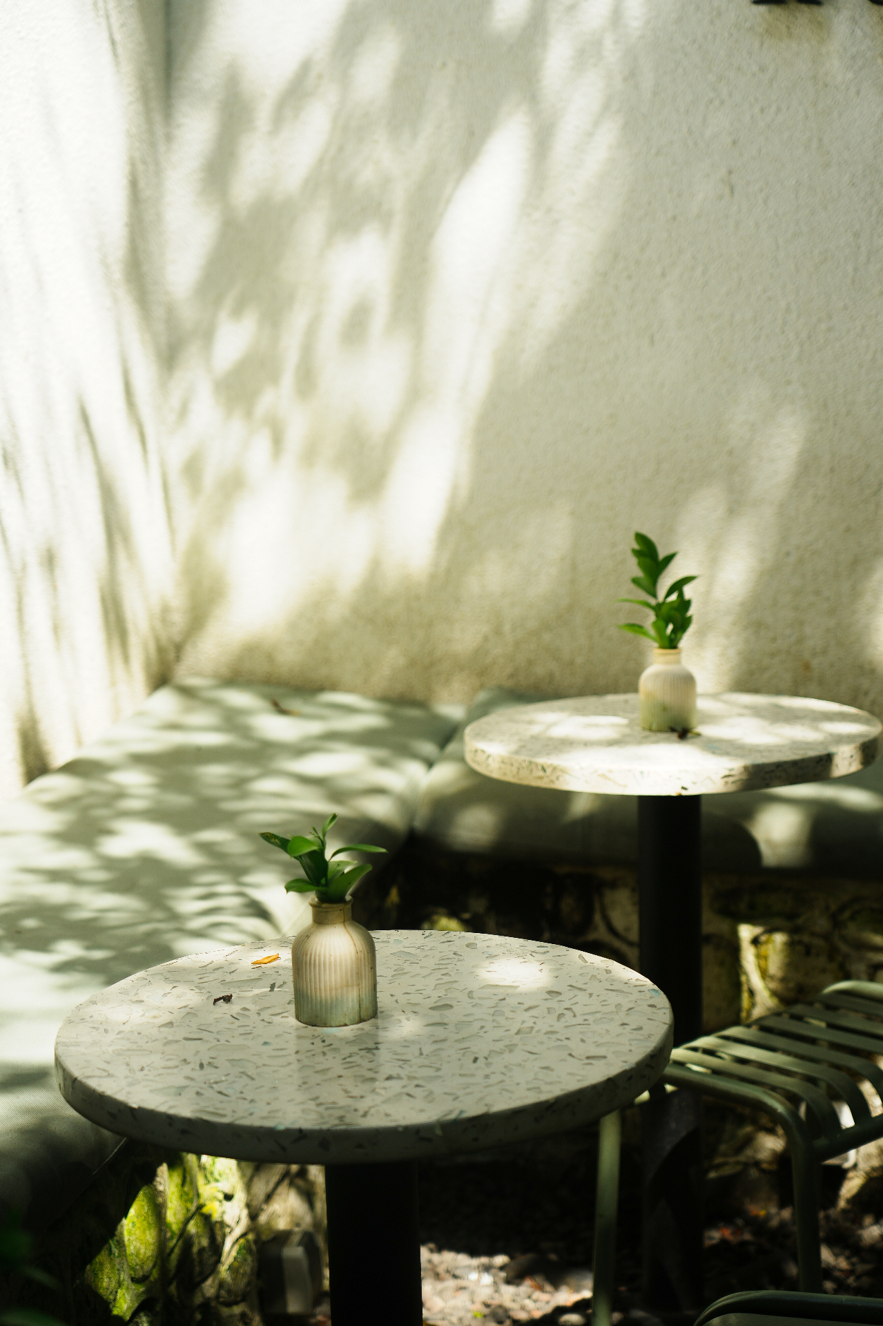 Terrazzo café tables in dappled afternoon light with sage banquette and small ceramic bud vases
