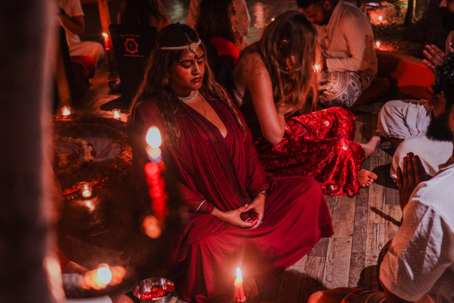 Woman in red sari meditating by candlelight at a tantra ceremony in Goa