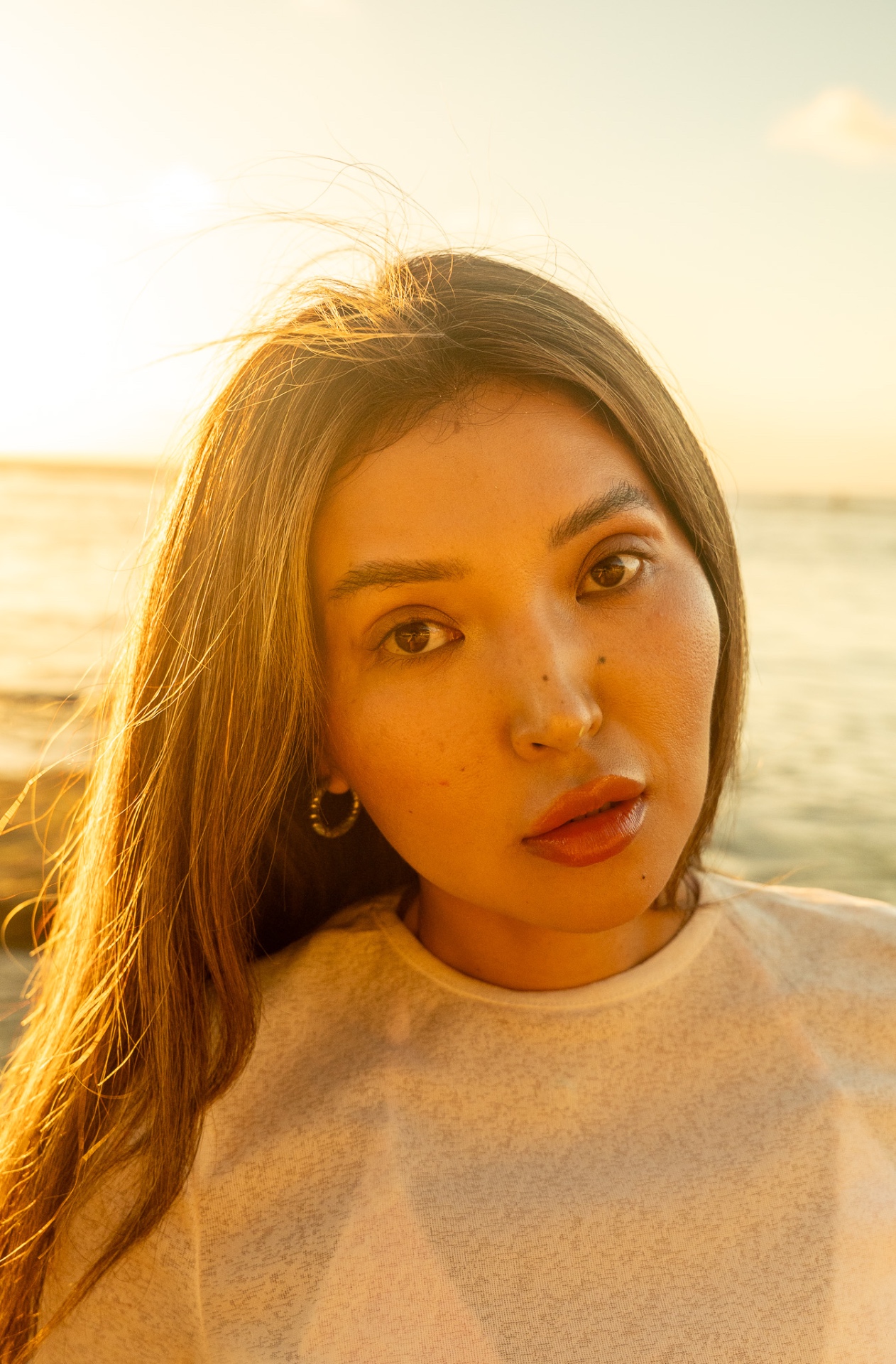 Backlit beauty portrait at golden hour, hair caught in sea breeze